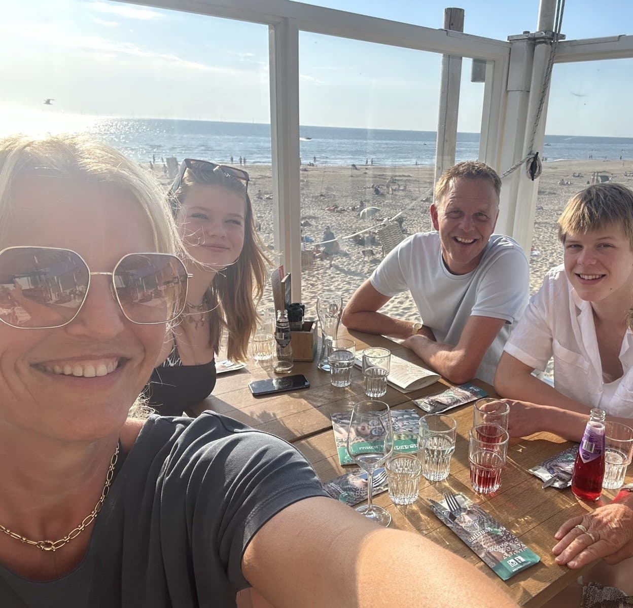 Familie aan tafel bij het strandpaviljoen, met het strand van Egmond op de achtergrond